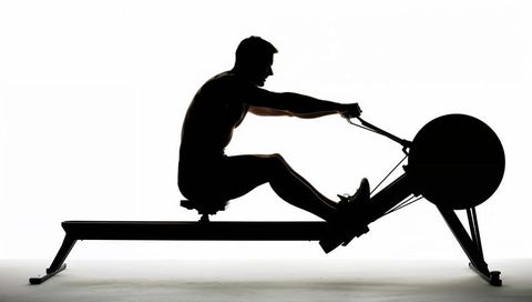 Silhouette male rowing on ergometer, backlit studio workout, minimalist fitness concept