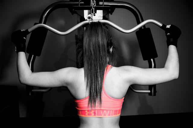 Fit woman using weight machine at gym for strength training. Highlights back muscles and athleticism. Ideal for fitness, health, and exercise content, gym promotions, workout motivation and sportswear advertisements.