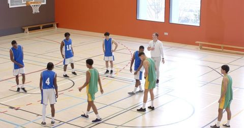 Diverse Basketball Team Intently listening to Coach Instruction in Sports Hall