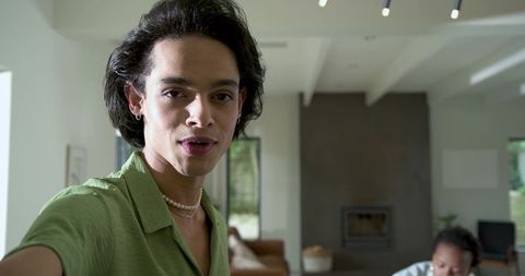 Young diverse man reaching toward camera in modern living room speaking to viewer