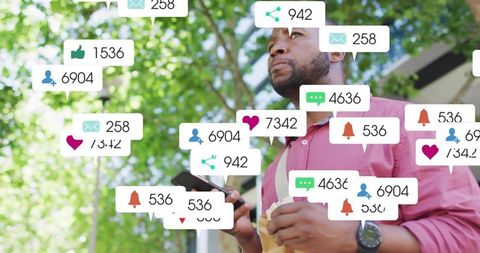 Man holding smartphone and coffee amid social media notifications under sunlit trees