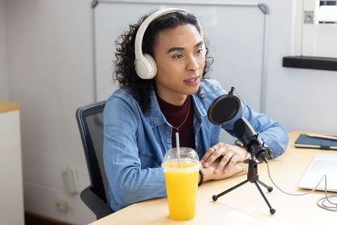 Non-binary creator podcasting at home desk with headphones, usb microphone and pop filter