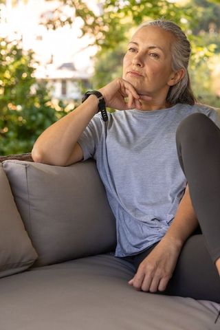 Mature woman relaxing on patio sofa, contemplative senior enjoying outdoor calm and sunlight