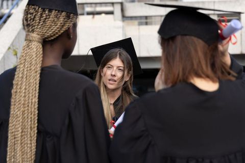 Graduates celebrating on campus, wearing mortarboards and holding red ribbon diplomas