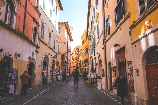 Narrow European street lined with colorful buildings and cobblestone path. People walking and enjoying the charming, historical ambiance. Ideal for projects about European travel, cultural experiences, historical architecture, and urban scenes.