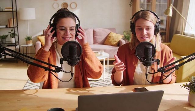 Recording cozy home podcast with two female hosts wearing headphones and talking engagingly