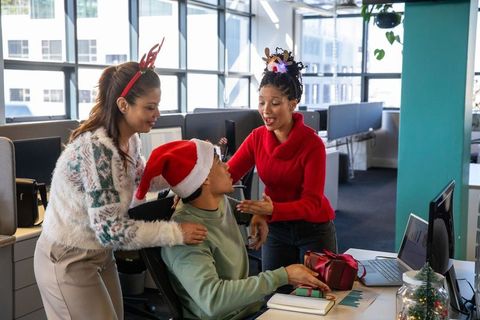 Multicultural coworkers celebrating holiday gift exchange at modern open-plan office desk
