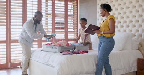 African American Family Packing Luggage on Bed Preparing for Vacation with Tablet