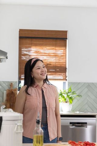 Asian woman smiling in cozy modern kitchen wearing pink sleeveless shirt and headband