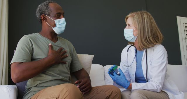 Caucasian senior female doctor holding medication talking with male patient in bed both wearing face masks. hygiene healthcare protection during coronavirus covid 19 pandemic.