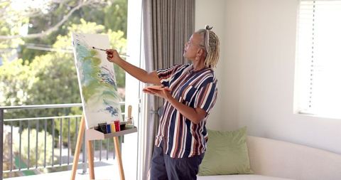 Senior woman painting vibrant canvas near sunlit window