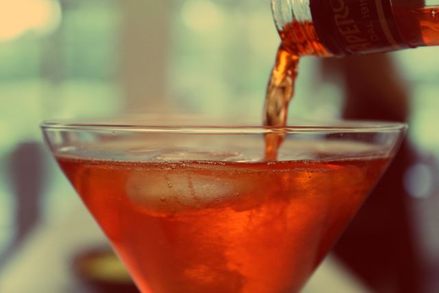 Close-up of Aperol Spritz being poured into a cocktail glass with ice. Ideal for illustrating refreshing summer cocktails, aperitifs, or beverage choices. Perfect for use in restaurant menus, bar advertisements, and social media promoting drink specials or alcoholic beverages.