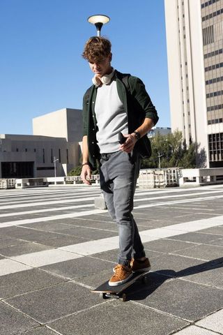 Riding skateboard commuting student with backpack and headphones across urban plaza