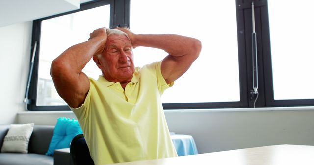 Elderly man seen clutching his head in frustration while inside a modern room. Can be used for concepts related to mental health, aging, stress, and emotional distress among the elderly. Suitable for articles or campaigns focusing on senior health and well-being, or awareness for mental health support services.