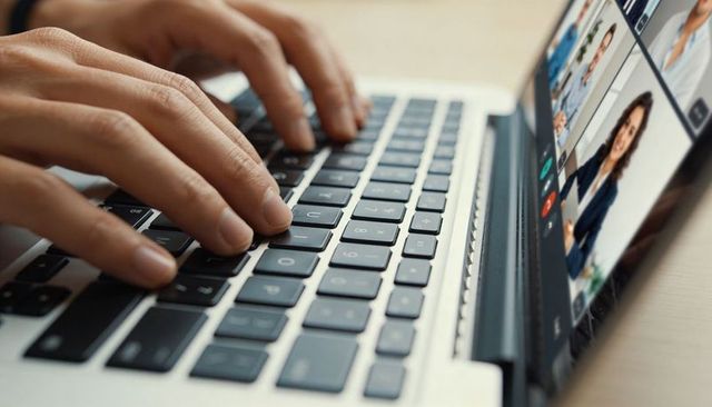 Hands typing on laptop keyboard during remote video meeting with professional participants