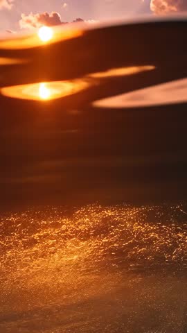 Vertical sunset video showing golden sun approaching horizon and glittering path on waves