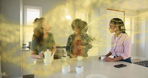 Three women chatting around modern kitchen island, enjoying tea, casual friendship moment