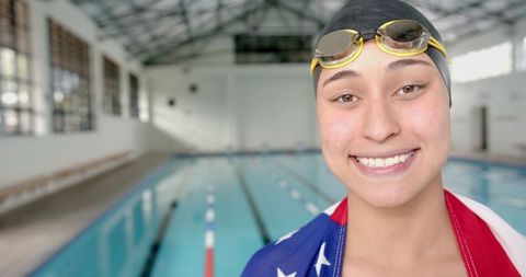 Smiling Female Swimmer Wearing Goggles with Flag by Indoor Swimming Pool