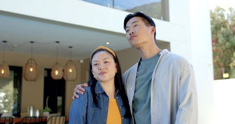 Modern asian couple embracing on bright terrace with rattan pendant lights and greenery
