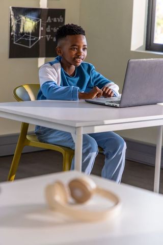 African American Preteen Typing on Laptop in Classroom with Headphones Nearby, Focused