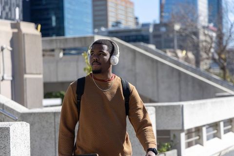 African american man walking urban plaza with longboard and headphones, commuter lifestyle
