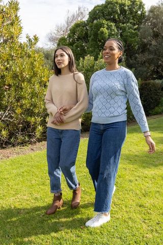 Diverse friends walking in park linking arms wearing sweaters and jeans, casual outdoors