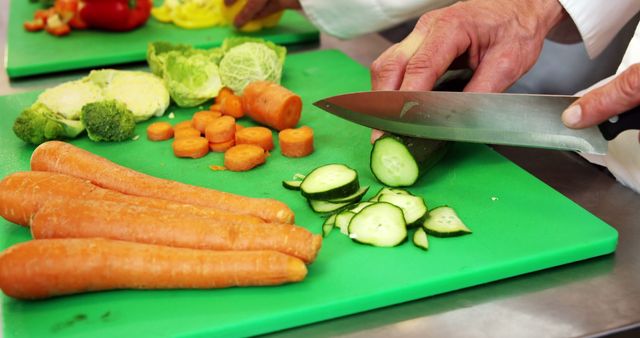 Chef slicing fresh vegetables, including carrots and cucumber, in a professional kitchen. This image highlights the preparation process in culinary settings and can be used for articles or advertisements related to cooking, healthy eating, culinary classes, or professional recipes.