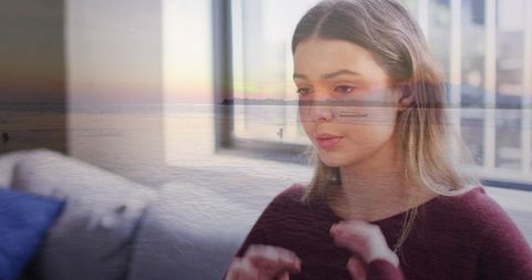Young woman typing on laptop with coastal sunset double exposure reflected through window