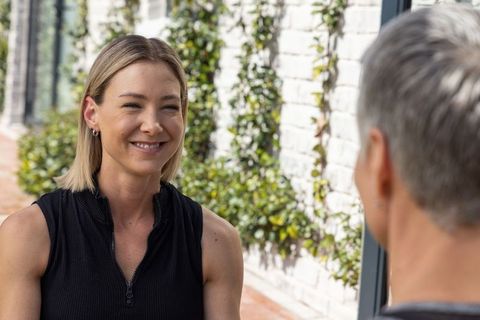 Young woman smiling during outdoor conversation with senior man on vine-covered patio