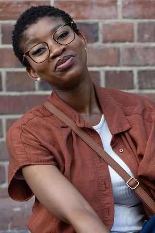 African american woman wearing rust shirt and glasses posing by brick wall