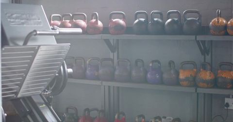 Kettlebells lining metal shelves beside leg press machine in industrial gym space