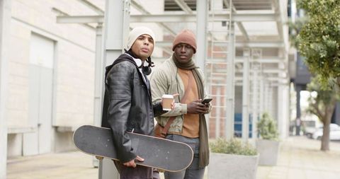 Diverse young men hanging out with skateboard and coffee on urban sidewalk, streetwear