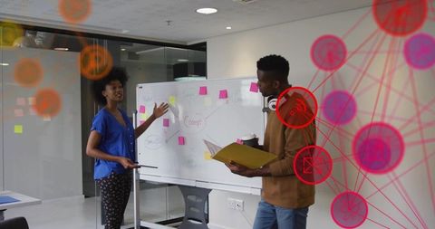 Colleagues brainstorming at whiteboard with sticky notes collaborating in modern glass office