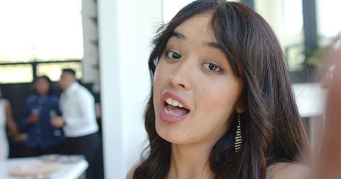 Asian woman talking to camera at reception wearing dangling rhinestone earrings, closeup