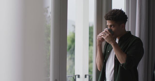 Thoughtful biracial man looking through the window and drinking coffee - Download Free Stock Photos Pikwizard.com