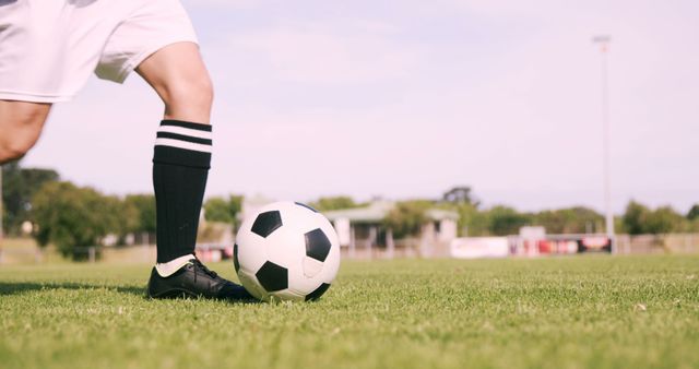 A young Caucasian soccer player is about to kick a soccer ball on a lush green field, with copy space. Capturing the moment right before action, the image conveys anticipation and the vibrant atmosphere of outdoor sports.