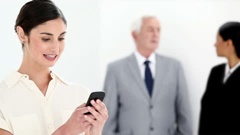 Businesswoman Engaged with Smartphone, Colleagues Blurred in Background