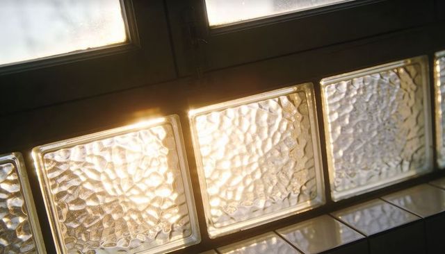 Warm sunlight streaming through textured glass blocks casting reflections on tile sill