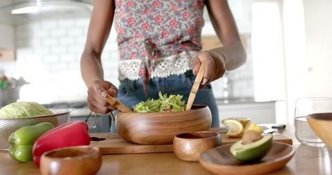 Woman preparing fresh salad with wooden utensils in kitchen