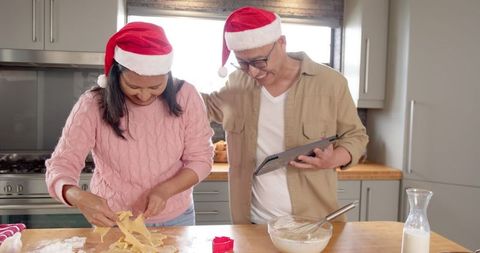 Diverse couple making holiday cookies using tablet