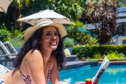 African american woman relaxing poolside wearing straw hat reading magazine on tropical resort