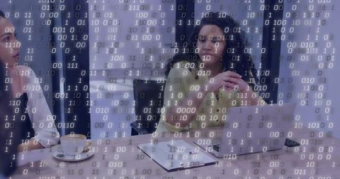 Female executive presenting at boardroom table with laptop, documents and binary data overlay