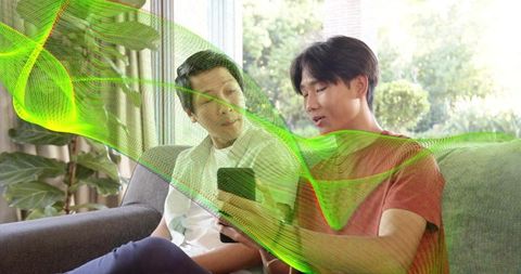 Teenager sharing smartphone with father on sunlit sofa with neon green data wave overlay