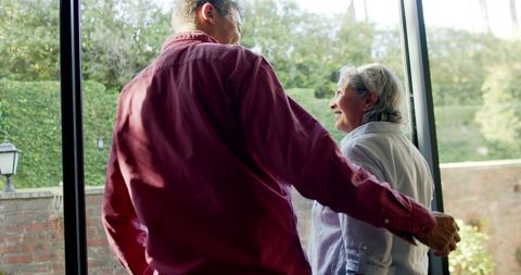 Senior Biracial Couple Embracing by Large Window at Home