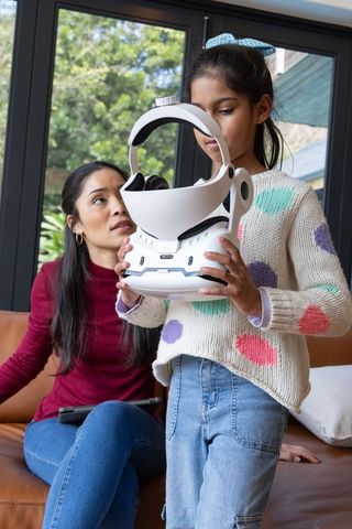 Asian mother and daughter exploring white vr headset in cozy living room with tablet