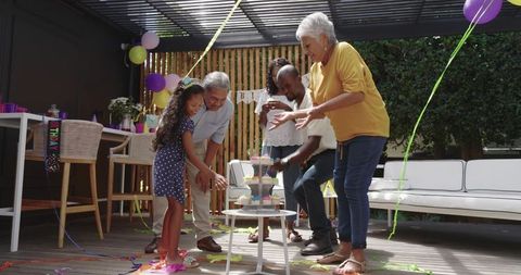 Multigenerational diverse family celebrating birthday with cupcakes on backyard pergola