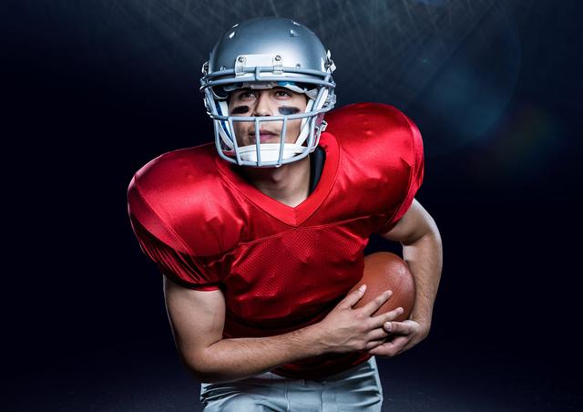 American football player holding red ball against black background
