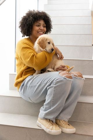 Smiling woman cuddling golden retriever puppy on modern sunlit stairs cozy home lifestyle