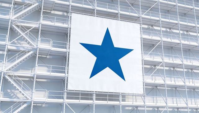 Large blue star banner hanging on white scaffolding facade with metal stairways