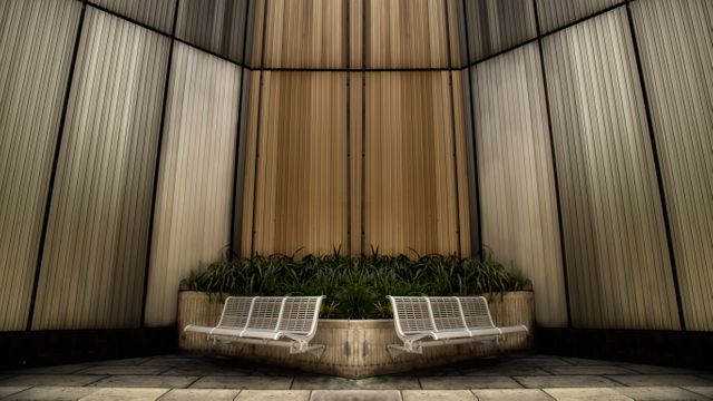 Symmetrical design features vertical panels creating a contemporary urban setting. White metal benches surround a central planter filled with greenery. Ideal for concepts related to modern architecture, public seating, relaxing outdoor areas, or city landscapes.